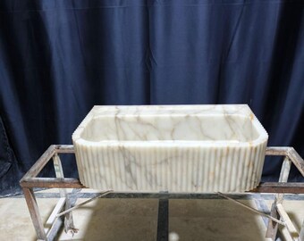 以下が含まれることがあります： 金属製のスタンドの上に置かれた、フルーテッドデザインの白い大理石のシンク。シンクは長方形で、滑らかで磨かれた表面をしています。