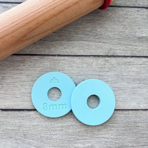 May include: Two light blue plastic rolling pin guides with an 8mm hole in the centre. The guide on the left has a small mountain icon on top.
