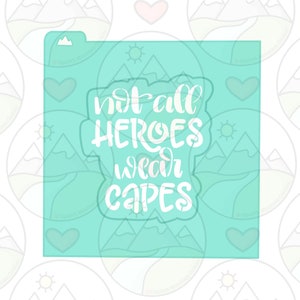 May include: A teal blue stencil with the text "Not all heroes wear capes" in white. The stencil is designed for crafting and decorating.