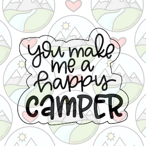 May include: A black and white cookie cutter in the shape of a speech bubble with the text "You make me a happy camper" inside.
