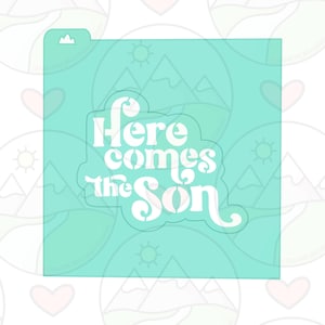 Peut inclure: Un pochoir bleu turquoise avec le texte "Here comes the sun" en blanc. Le texte est dans un style de police rétro.