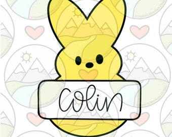 May include: A yellow bunny-shaped cookie with a heart on its chest and a banner that says "Colin".