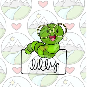 Puede incluir: Un cortador de galletas de gusano verde con gafas redondas y una cara sonriente. El cortador sostiene un cartel que dice "lilly".