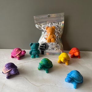 May include: A set of non-toxic crayons shaped like turtles and a bear. The crayons are in a rainbow of colours, including purple, pink, orange, yellow, green, blue, and teal. The crayons are packaged in a clear plastic bag with a white paper label that reads "hand made" and "Non-toxic Crayons" and "Etsy: BrightSideStorefront".