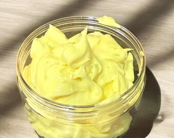 May include: A clear glass jar filled with a bright yellow, creamy substance. The substance is thick and appears to be a lotion or cream.
