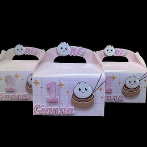 May include: Three pink party favor boxes with a dumpling theme. Each box features the number "1", the name "Gianna", and a cartoon dumpling illustration. The boxes have a handle with the word "one" on them.