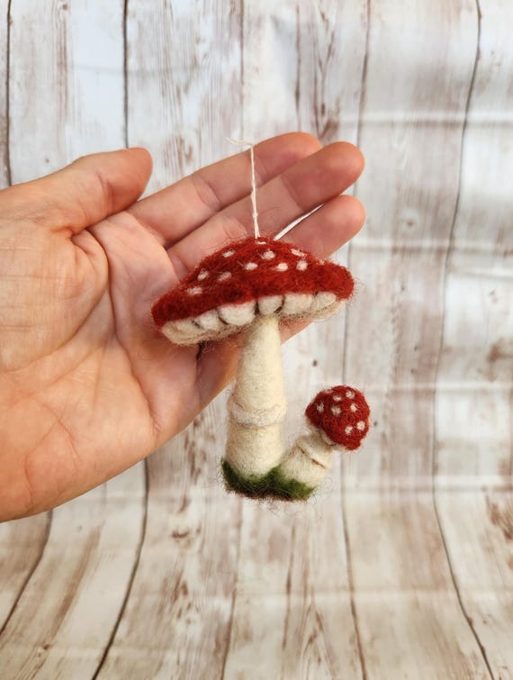 A needle-felted Amanita muscaria mushroom ornament sculpted by hand — tiny, tactile, and wildly detailed in a way that makes it feel more like a museum piece than a Christmas ornament.