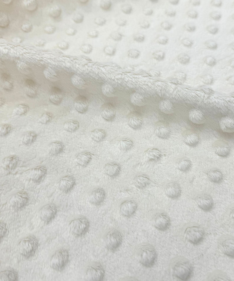 May include: White plush fabric with a textured dot pattern. The fabric is soft and has a subtle sheen.