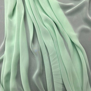 May include: A light green fabric with a soft, flowing texture. The fabric is draped and folded, creating a smooth, elegant look.