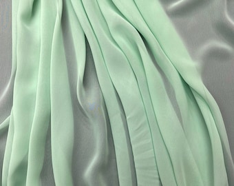 May include: A light green fabric with a soft, flowing texture. The fabric is draped and folded, creating a smooth, elegant look.