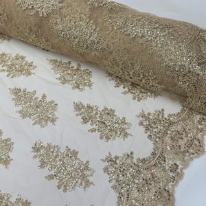 May include: Beige lace fabric with a delicate floral pattern and gold sequins. The lace has a scalloped edge.