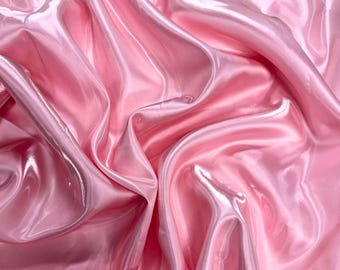 May include: A close-up shot of a luxurious, flowing fabric in varying shades of pink. The material has a glossy, satin-like sheen, with soft folds and gentle curves that create a sense of depth and movement. The overall effect is smooth and elegant.