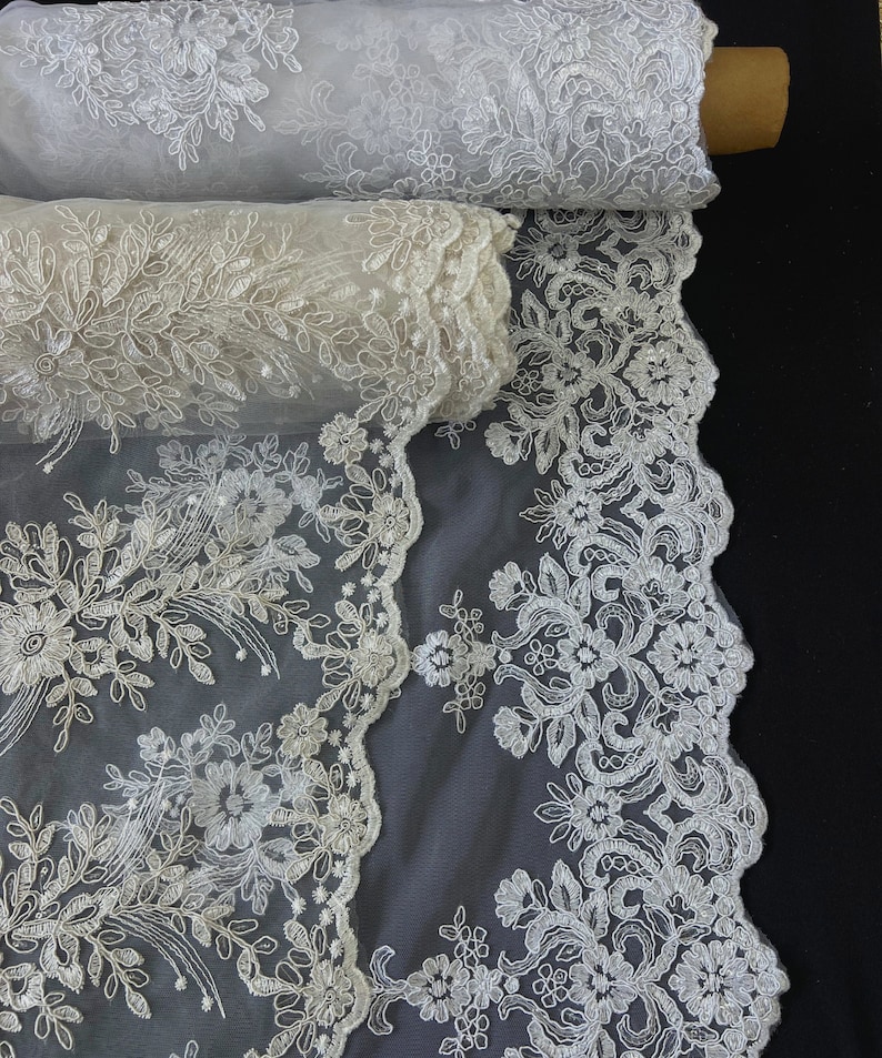 May include: White floral lace fabric with a delicate pattern. The lace is rolled up and the fabric is sheer and lightweight.