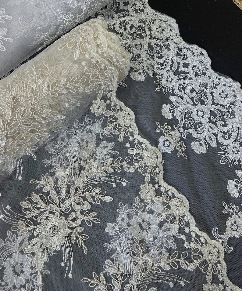 May include: White floral lace trim with a scalloped edge. The lace is delicate and intricate, with a floral pattern.