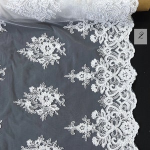 May include: White floral lace fabric with a scalloped edge. The lace is delicate and intricate, with a repeating pattern of flowers and leaves.