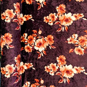 May include: Burgundy velvet fabric with a floral pattern featuring orange and cream flowers. The fabric has a textured, crushed velvet look.