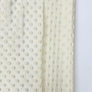 May include: A close-up of two pieces of white fabric with a textured, dotted pattern. The fabric is soft and plush, and would be ideal for making blankets, pillows, or other home decor items.