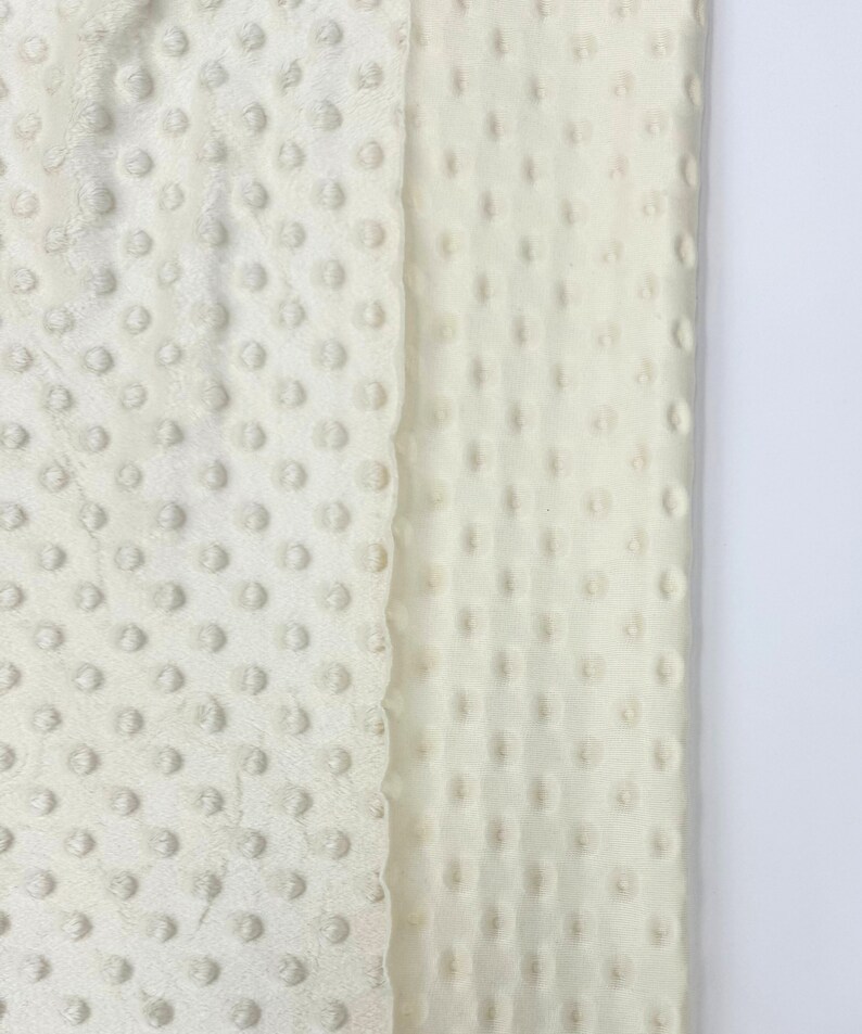 May include: A close-up of two pieces of white fabric with a textured, dotted pattern. The fabric is soft and plush, and would be ideal for making blankets, pillows, or other home decor items.