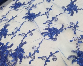 Puede incluir: Primer plano de una tela de encaje azul real. La tela presenta un intrincado diseño de bordado floral con flores detalladas y vides arremolinadas. El encaje es un material transparente, lo que permite que el fondo sea visible a través del delicado patrón.