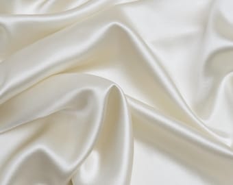 May include: A smooth, white satin fabric with soft, flowing folds. The fabric is luxurious and elegant, with a subtle sheen.