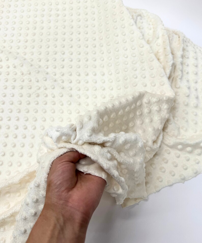 May include: White plush fabric with a textured dot pattern. The fabric is soft and fluffy, and it would be perfect for making blankets, pillows, or other home decor items.