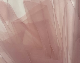 Puede incluir: Primer plano de una tela de tul rosa polvoriento suave y transparente. La tela está drapeada y doblada, creando una textura delicada y aireada.
