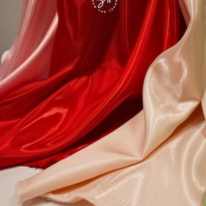 May include: Close-up of flowing, shiny fabric in shades of red and blush pink. The fabric has a smooth, satin-like texture, with visible folds and highlights. The logo "Sew the Trend" is visible in the upper center.