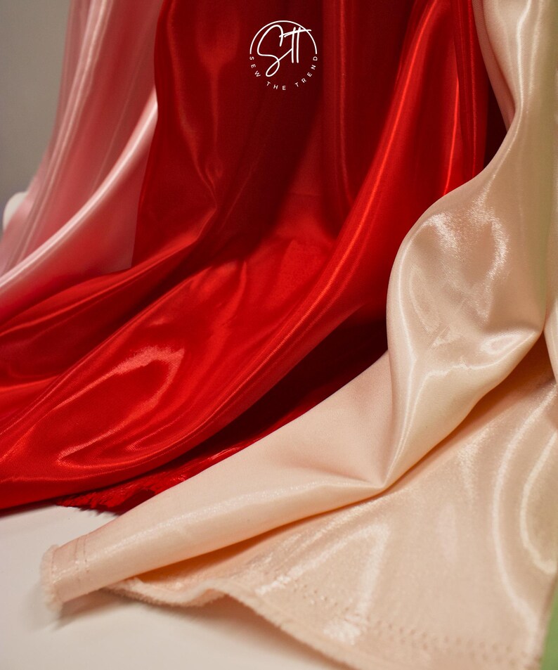 May include: Close-up of flowing, shiny fabric in shades of red and blush pink. The fabric has a smooth, satin-like texture, with visible folds and highlights. The logo "Sew the Trend" is visible in the upper center.