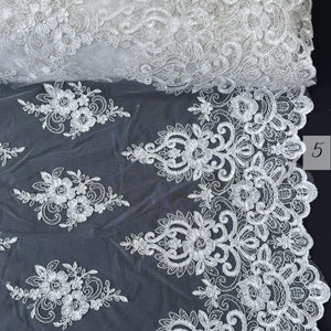 May include: White lace fabric with a floral pattern. The lace is delicate and intricate, with a scalloped edge. The fabric is sheer and lightweight, making it ideal for a variety of projects.