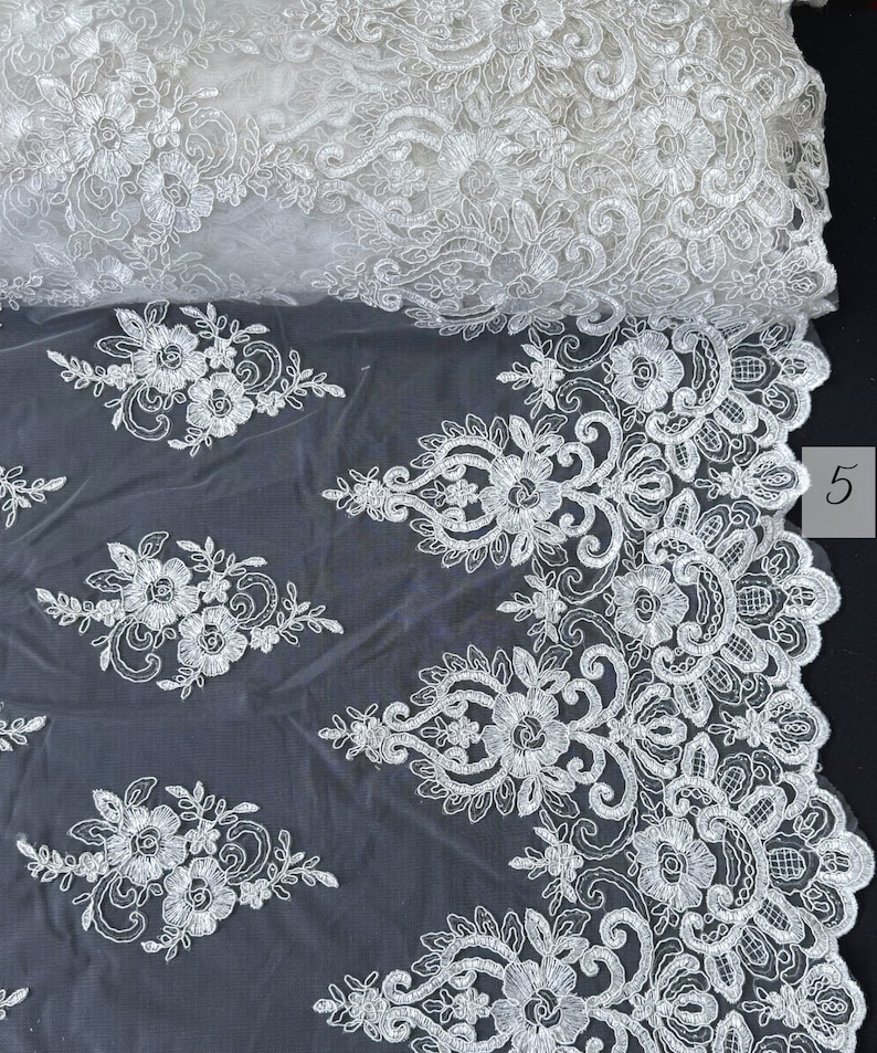 May include: White lace fabric with a floral pattern. The lace is delicate and intricate, with a scalloped edge. The fabric is sheer and lightweight, making it ideal for a variety of projects.