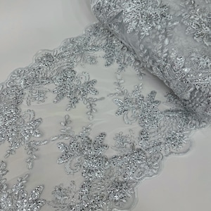 May include: Silver beaded lace fabric with a floral design. The lace is delicate and intricate, with small beads scattered throughout.