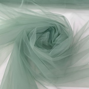 May include: A roll of soft, sage green tulle fabric. The tulle is delicate and sheer, with a slightly crinkled texture.