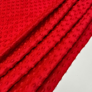May include: Red minky fabric with a textured dot pattern. The fabric is folded in layers, showing the soft texture.