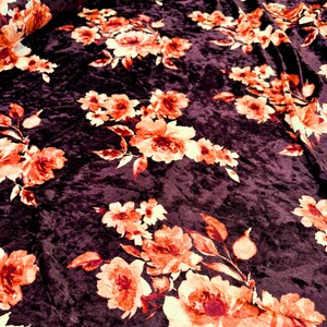 May include: Close-up of a dark purple velvet fabric with a floral pattern. The flowers are orange and yellow with a white outline. The fabric has a soft, plush texture.