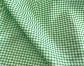 May include: Close-up of a green and white gingham fabric. The fabric is folded, showing the pattern's texture and the interplay of light and shadow. The classic check pattern is evenly spaced and creates a visually appealing design.
