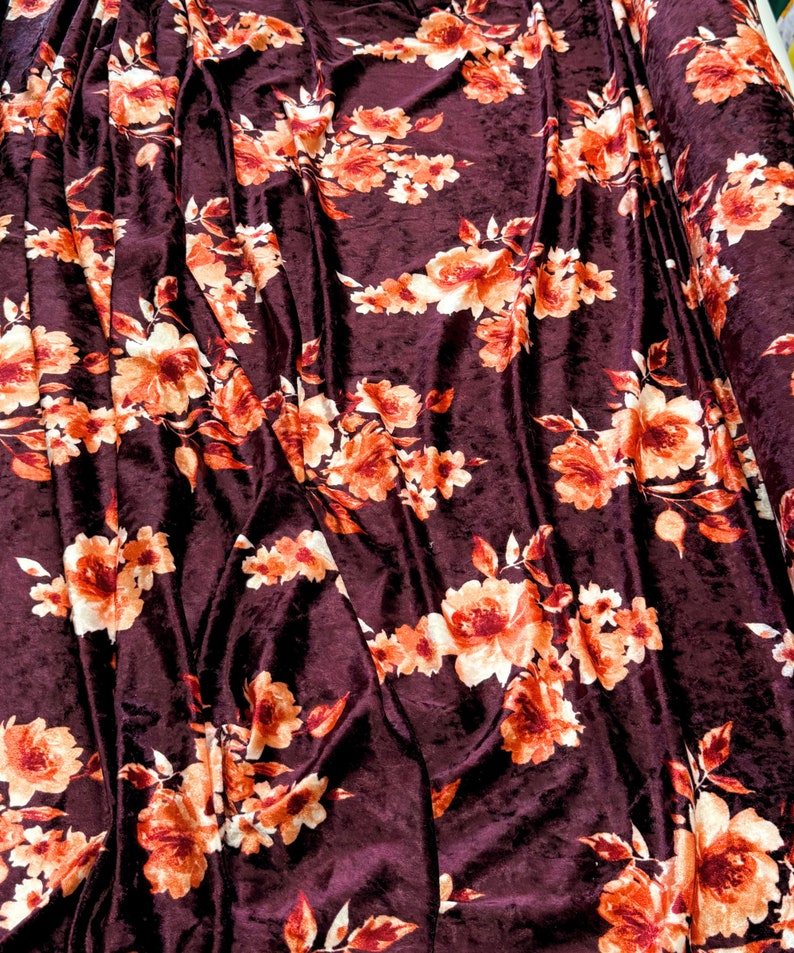 May include: Burgundy velvet fabric with a floral pattern in shades of orange and white. The fabric has a soft, plush texture.