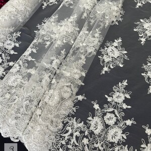 May include: White floral lace fabric with a delicate pattern. The lace is on a sheer mesh background.