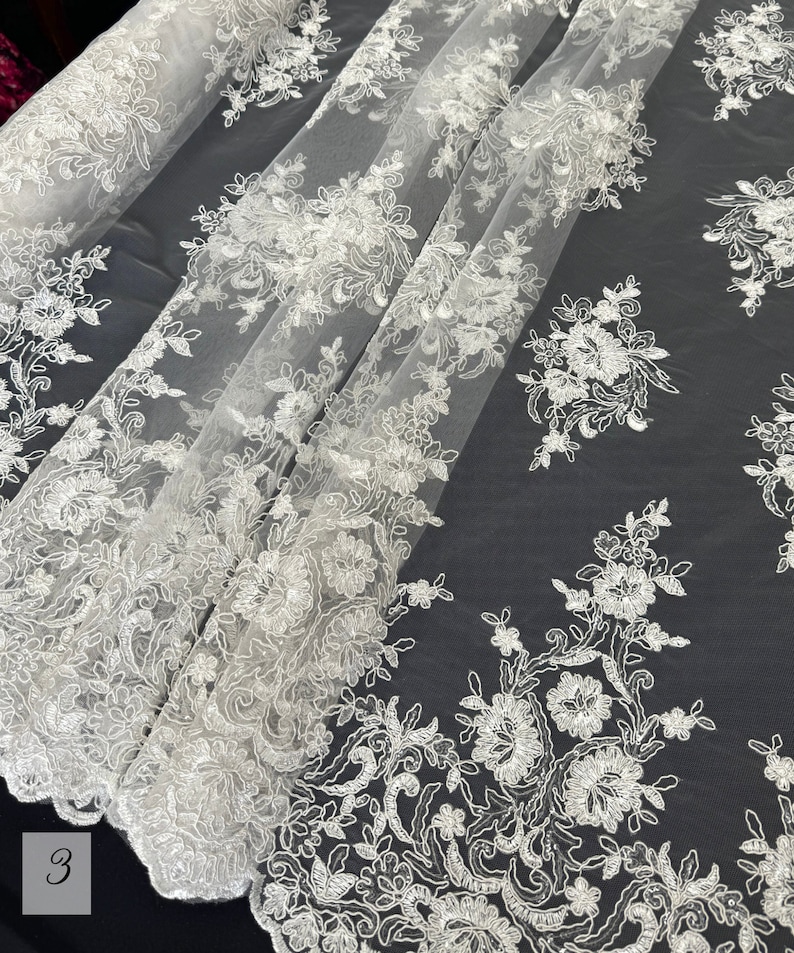 May include: White floral lace fabric with a delicate pattern. The lace is on a sheer mesh background.