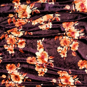 May include: Burgundy velvet fabric with a floral pattern in shades of orange and cream. The fabric is draped and folded, showing the texture of the velvet.