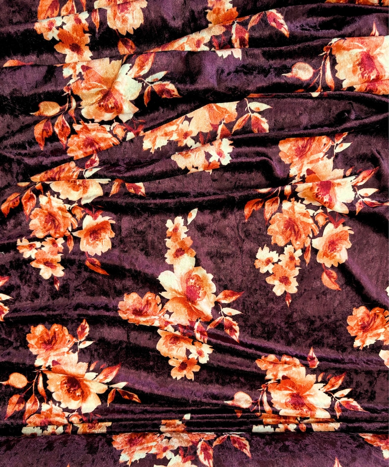 May include: Burgundy velvet fabric with a floral pattern in shades of orange and cream. The fabric is draped and folded, showing the texture of the velvet.