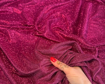 Pode incluir: Close-up de um tecido magenta vibrante com uma textura brilhante e cintilante. O tecido está drapeado e dobrado, criando sombras e destaques. O material parece macio e fluido, adequado para vestuário ou projetos decorativos.