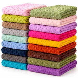 May include: Stacks of colorful, plush blankets in various shades, including pink, green, yellow, and blue. Each blanket has a textured, dotted surface. The blankets are neatly folded, showcasing a variety of colors.