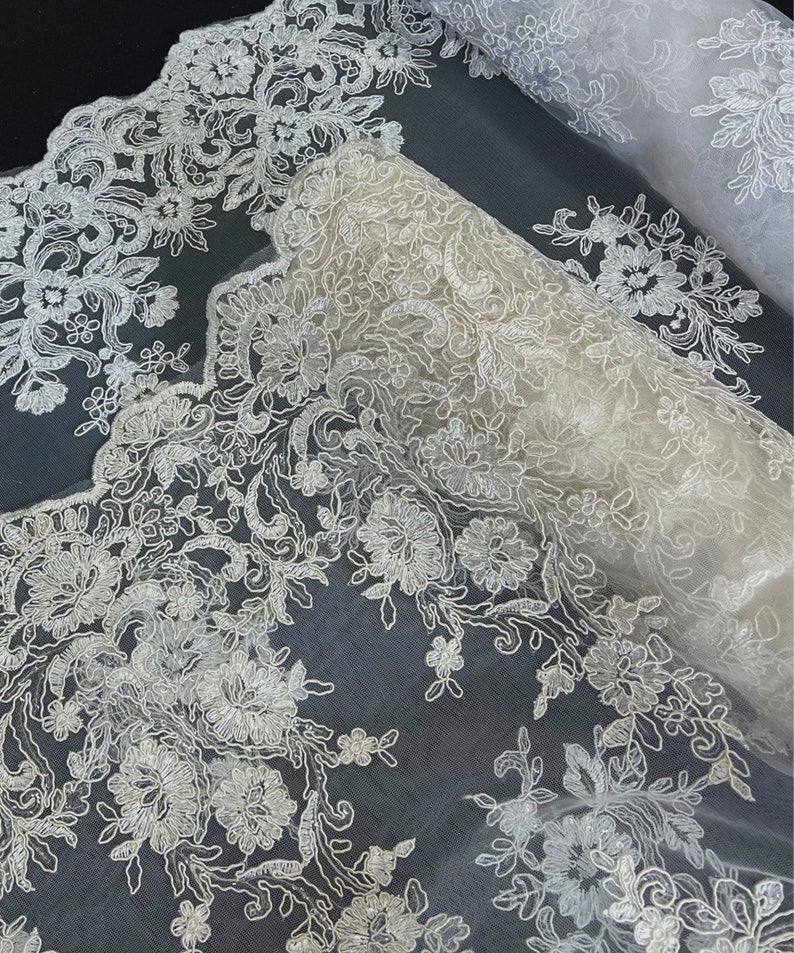 May include: White lace fabric with a delicate floral pattern. The lace is on a sheer mesh background.