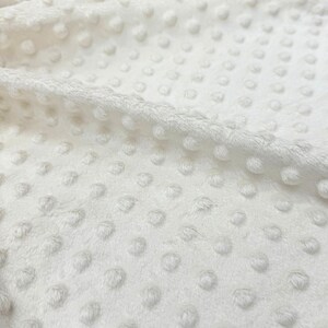 May include: Close-up of a white, textured fabric with small, raised dots. The fabric has a soft, plush feel.