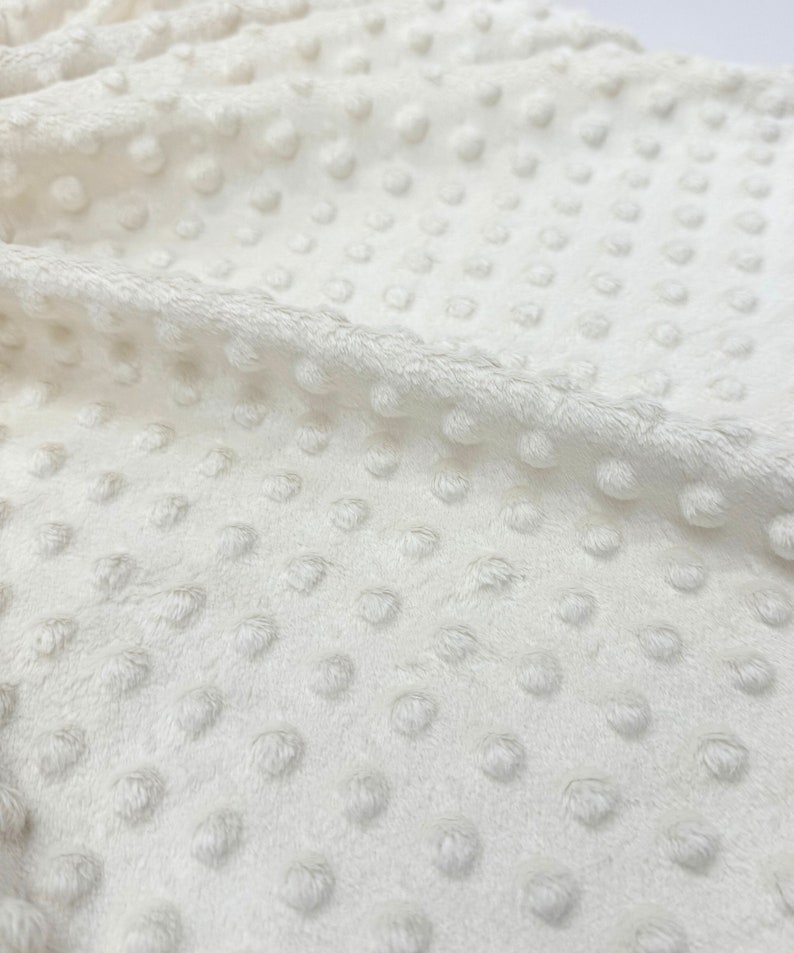May include: Close-up of a white, textured fabric with small, raised dots. The fabric has a soft, plush feel.