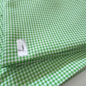 May include: Lime green and white gingham fabric. The fabric is folded, showing the pattern of small, evenly spaced squares. A tag with the word "LIME" is attached to the fabric.