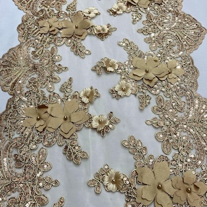 May include: Gold lace fabric with 3D floral embellishments. The fabric features a delicate mesh base with gold sequins and intricate floral patterns. The 3D flowers are made of a soft, textured material and are accented with small pearl-like beads.