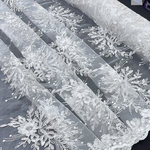 May include: White floral lace fabric with a delicate pattern. The lace is sheer and has a soft, flowing texture.