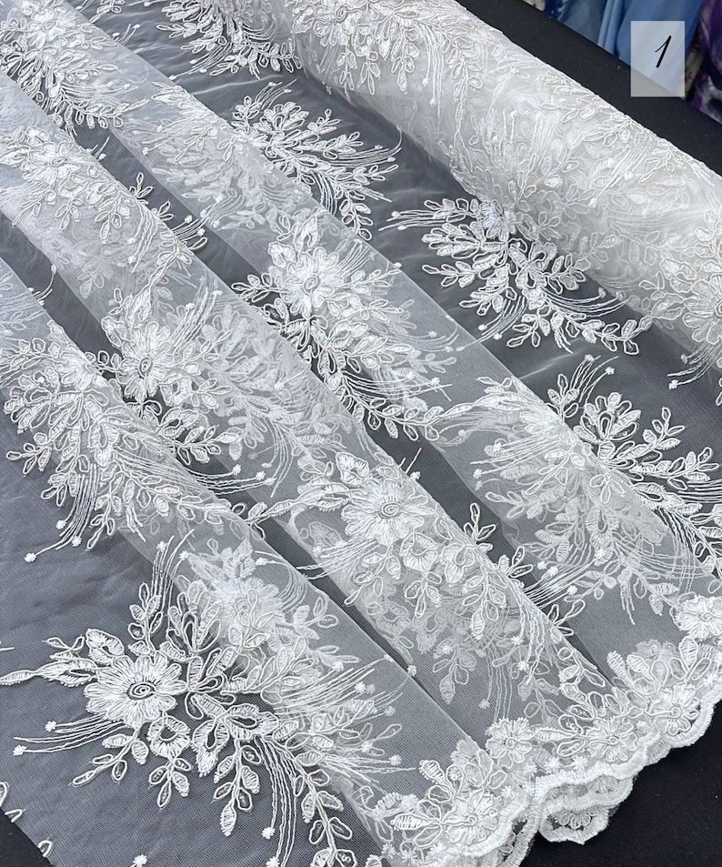May include: White floral lace fabric with a delicate pattern. The lace is sheer and has a soft, flowing texture.