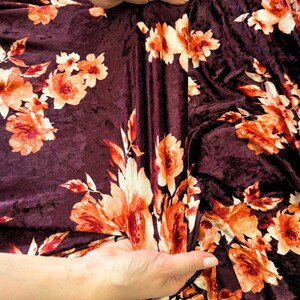 May include: Burgundy velvet fabric with a floral print in shades of orange and white. The fabric is soft and has a subtle sheen.